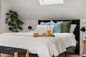 Ein ordentlich bezogenes Bett mit einem Frühstücksbrettchen, einem Nachttisch und einer großen Pflanze in einem modernen Schlafzimmer.