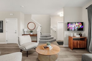 A modern living room with a grey sofa, a round coffee table, a TV displaying 'Smart TV', and a staircase leading to another level. - Family Getaway | Glacier Ridge | Calgary NW (Calgary)