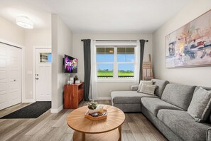 A modern living room with a grey sofa, a round wooden coffee table, a flat-screen TV, and a large abstract painting on the wall. - Family Getaway | Glacier Ridge | Calgary NW (Calgary)