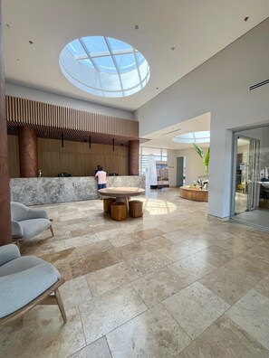 Eine geräumige Lobby mit rundem Tisch in der Mitte, Sitzgelegenheiten und einem großen Oberlicht.