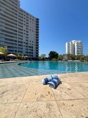A swimming pool with a towel, surrounded by a tiled deck, and tall buildings in the background. - Cozy 1-bedroom Apartment - Condo Sea + Mountain Views (Santa Marta)