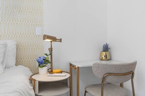 Ein ordentlich eingerichtetes Hotelzimmer mit einem Bett, einem Nachttisch mit Lampe, einem Sessel und einem kleinen Tisch mit Pflanze.