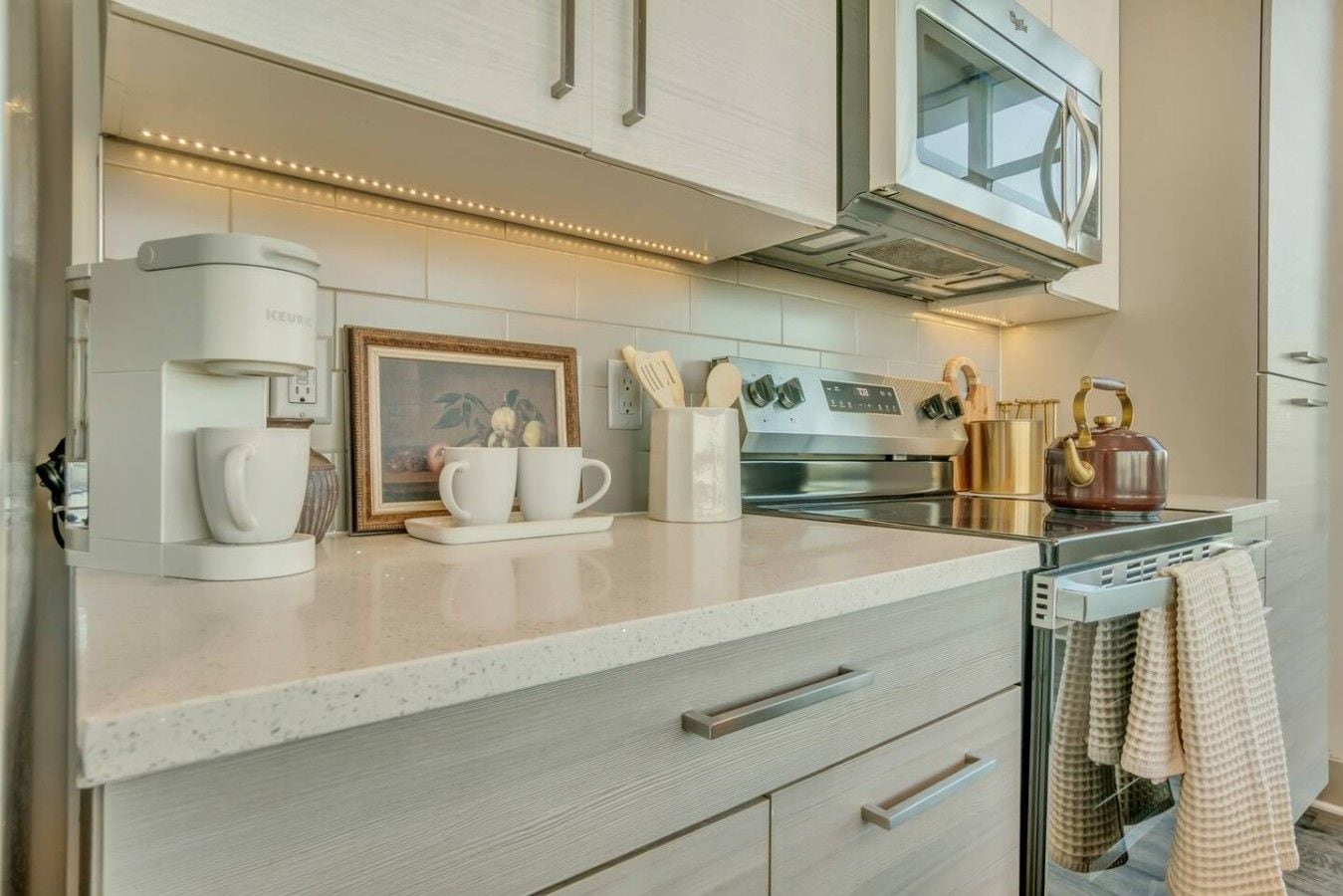 A modern kitchen with a built-in coffee maker, a framed picture, and a kettle on the counter.