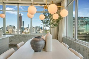 Un comedor moderno con vista a la ciudad, una mesa con jarrones y lámparas colgantes esféricas.