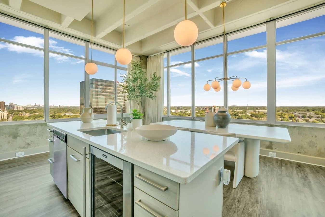 A modern kitchen with a large island, a dishwasher, and a view of the city through large windows.