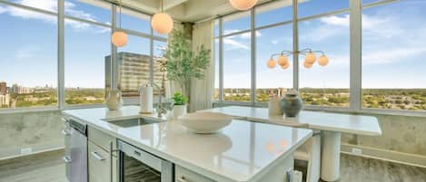 Une cuisine moderne dotée d’un grand îlot central, d’un lave-vaisselle et offrant une vue sur la ville grâce à de grandes fenêtres.