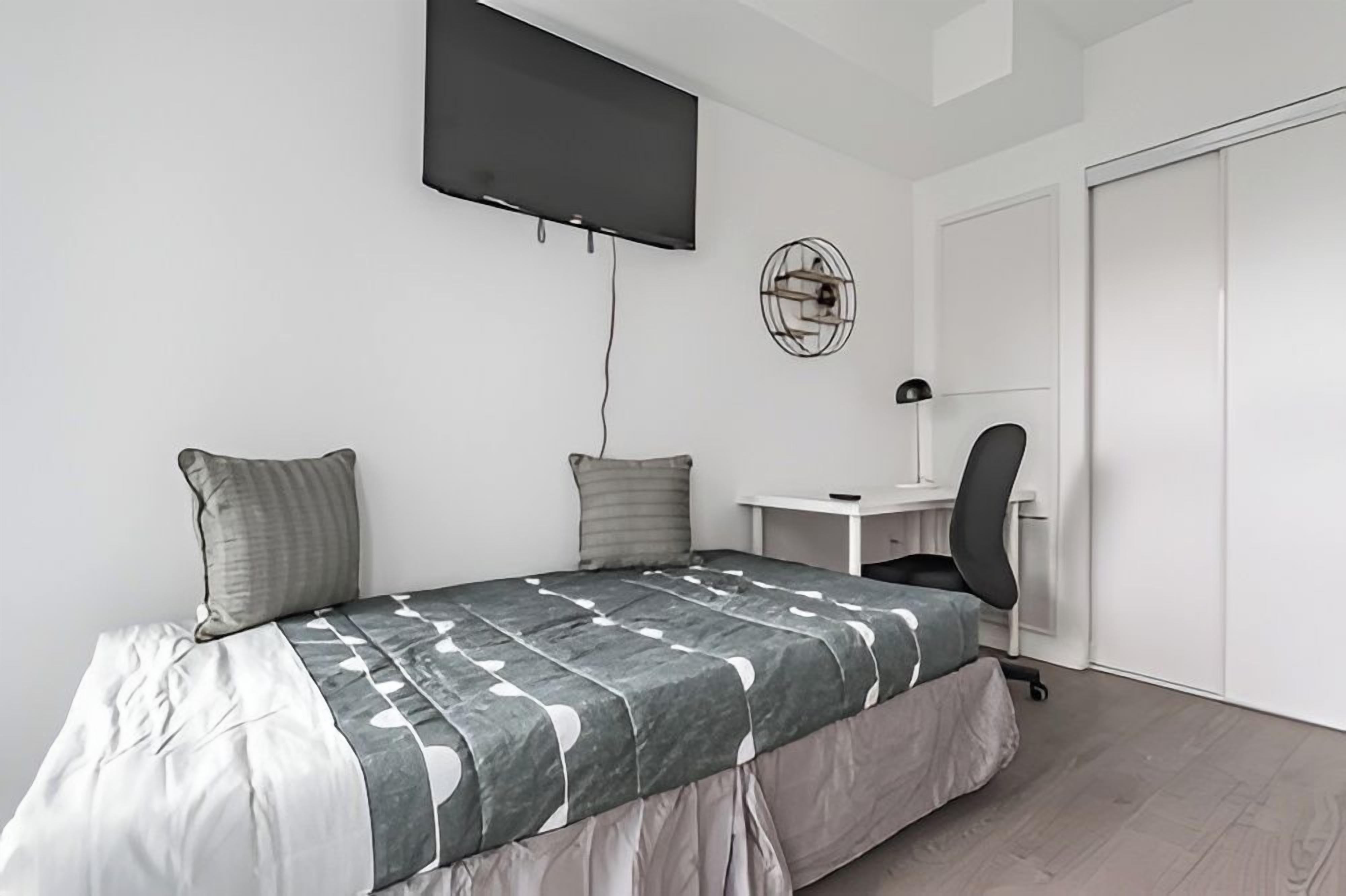 A bedroom with a bed, a desk, a chair, a TV, and a wardrobe.