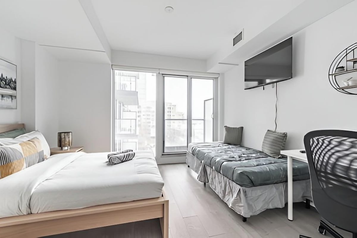 A modern bedroom with a bed, a desk, a chair, and a TV.