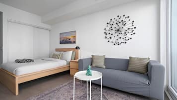 A modern bedroom with a bed, a grey sofa, a small white table, and a wall art piece.