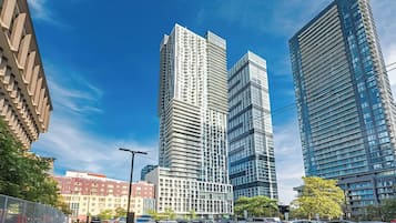 A cityscape with modern high-rise buildings, a clear sky, and a street with parked cars.