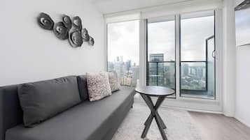 A modern living room with a gray sofa, patterned pillows, a round coffee table, and a city view through large windows.