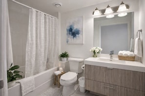 A modern bathroom with a bathtub, toilet, sink, and a large mirror. - The Boutique Suites - Jarvis Street (Toronto)