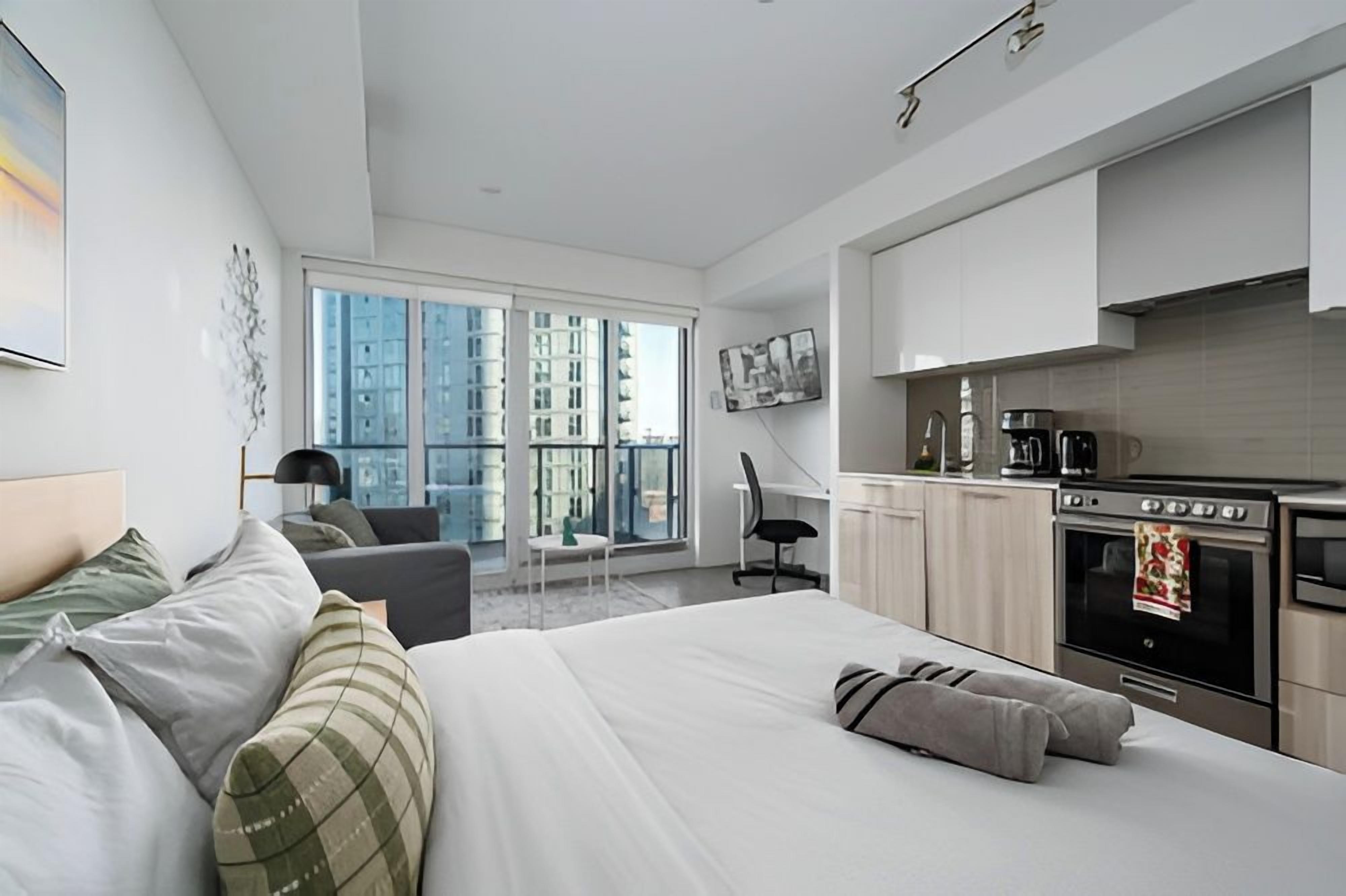 Una habitación de hotel moderna con una cama grande, un escritorio, una kitchenette y vistas a la ciudad.