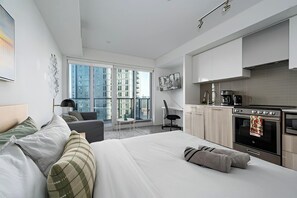 Una habitación de hotel moderna con una cama grande, un escritorio, una kitchenette y vistas a la ciudad.