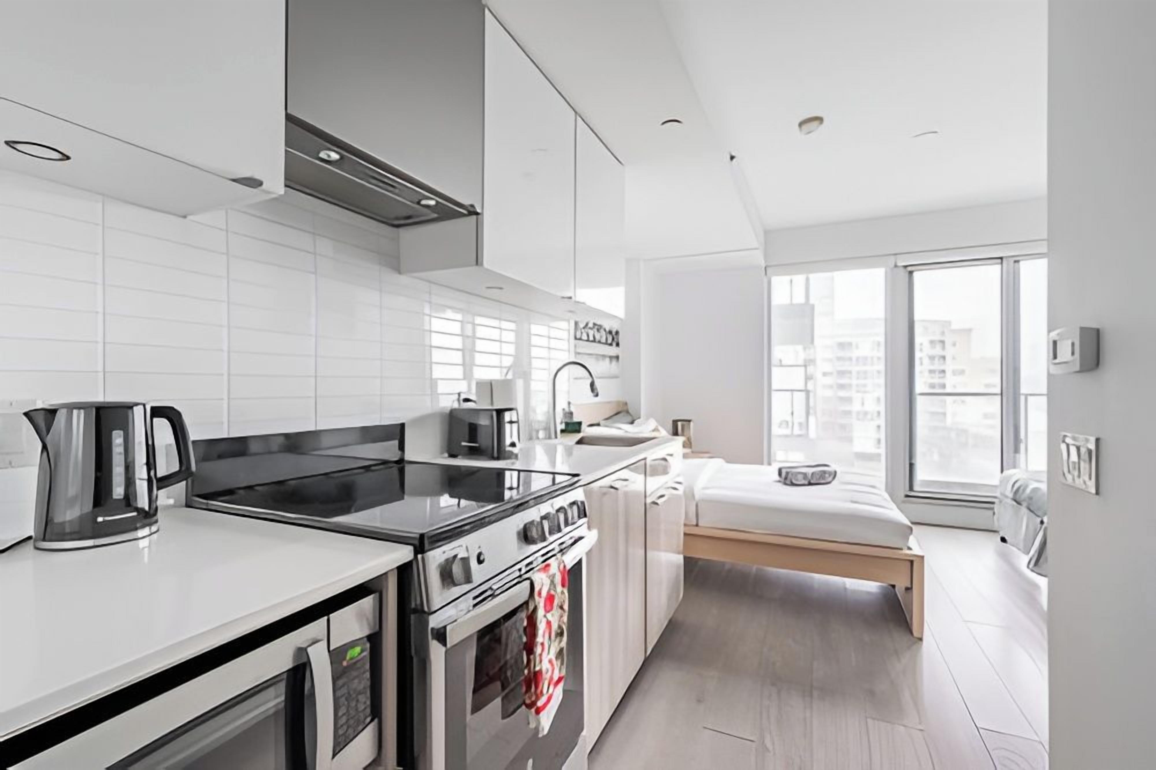 A modern kitchen with a stove, oven, and kettle, a small dining area, and a bed with a view.