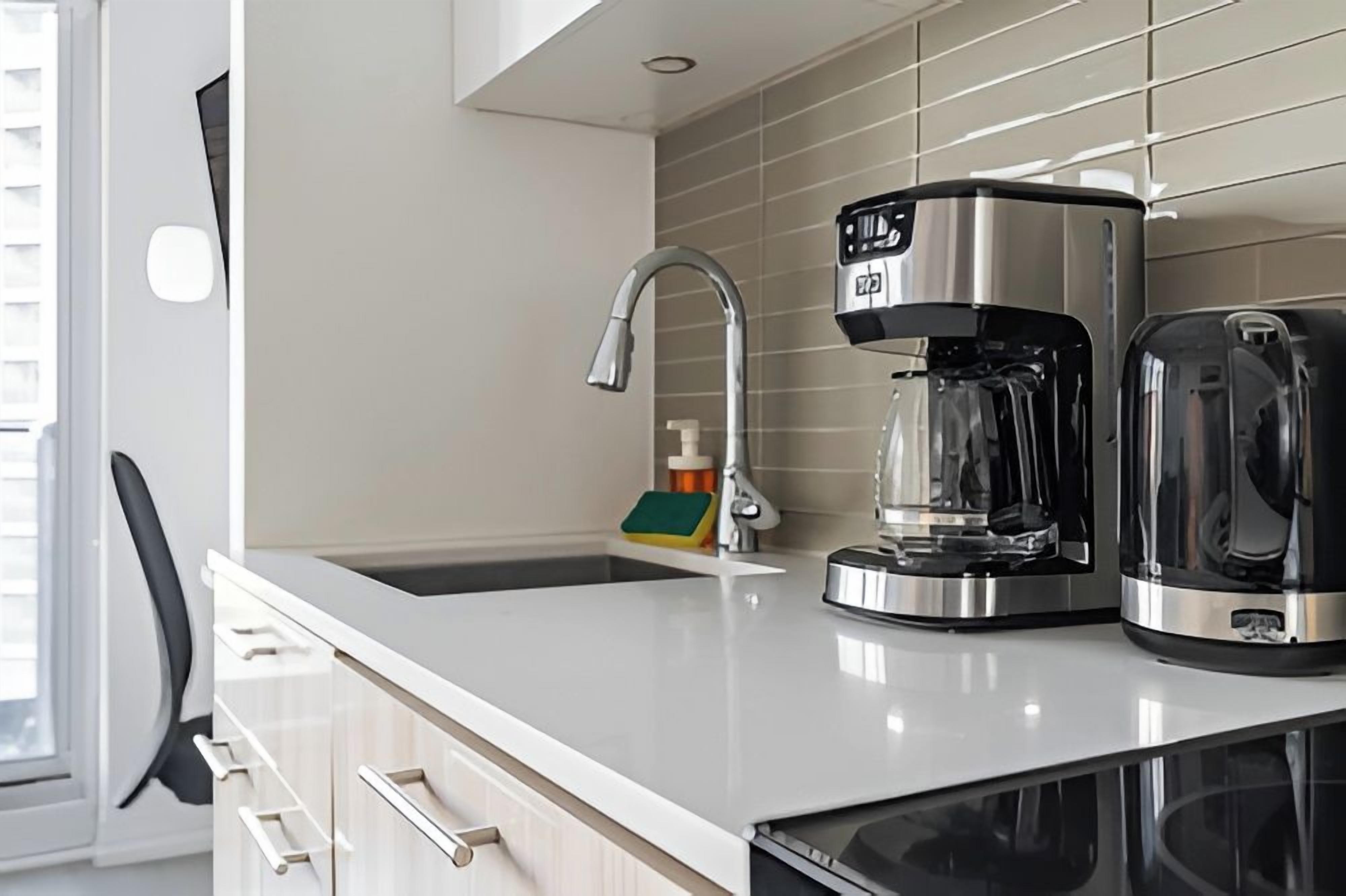 Una cocina moderna con una cafetera de acero inoxidable, una jarra de vidrio y un fregadero.