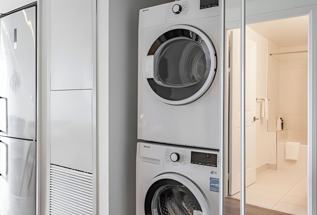 Una lavadora y secadora apiladas en un baño moderno con una zona de ducha visible.
