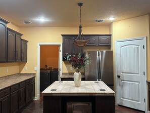 A kitchen with dark wooden cabinets, a stainless steel refrigerator, a tiled island, and a hanging light fixture. - LAKE view 4-bedroom HOmE with GAME Room (San Antonio)