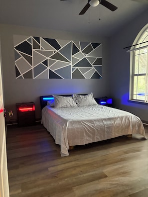 A bedroom with a bed, nightstands, a ceiling fan, and a geometric wall decoration. - LAKE view 4-bedroom HOmE with GAME Room (San Antonio)