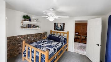 Une chambre à coucher avec un lit en bois, un ventilateur de plafond, un mur en pierre et une porte donnant sur une autre pièce.