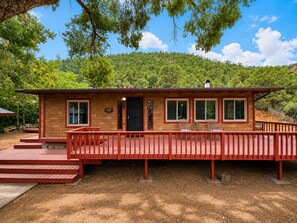 A wooden cabin with a deck, a front door, and windows.