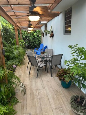 Une terrasse extérieure dotée d’une pergola en bois, de ventilateurs de plafond, d’une table avec des chaises et de plantes en pot.