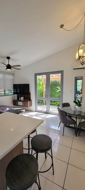 A modern kitchen with a dining area, a TV, and a view of a garden through glass doors. - * * CASA PALMA * *  Beachside Tropical Oasis (Ensenada)