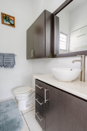 Une salle de bain avec un lavabo blanc, des meubles sombres, un miroir et un porte-serviettes.