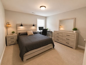 Een slaapkamer met een bed, nachtkastjes, een bureau, een dressoir en een spiegel.