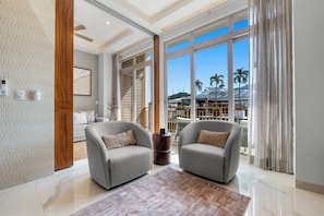 A modern living room with two grey armchairs, a patterned rug, and a large window with a view of palm trees and a building. - Penthouse 1BR | Rooftop Pool, Hot Tub & Romantic Zone (Puerto Vallarta)