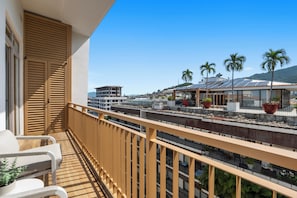 A balcony with a view of a cityscape, including buildings and palm trees. - Penthouse 1BR | Rooftop Pool, Hot Tub & Romantic Zone (Puerto Vallarta)