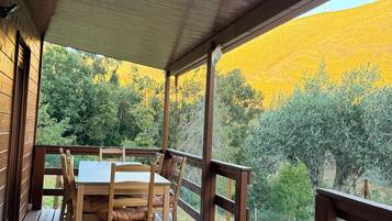 Una terraza de madera con una mesa y sillas, con vista a un paisaje natural con árboles y una colina.