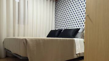 Une chambre à coucher avec un lit, un plancher en bois, une fenêtre avec des rideaux et un mur à motifs.