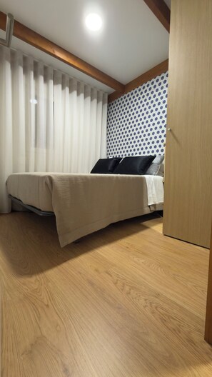 Ein Schlafzimmer mit einem Bett, Holzboden, einem Fenster mit Vorhängen und einer Wand mit Muster.