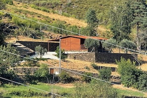 A rustic cabin with a stone foundation, surrounded by a dry, hilly landscape with sparse vegetation.