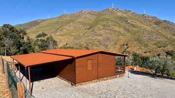 A wooden building with a sloped roof, surrounded by a stone-paved area and a green fence.