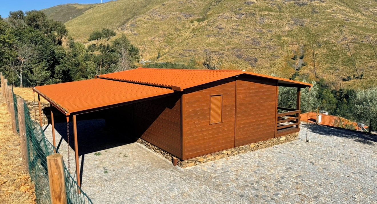 A wooden building with a sloped roof, situated on a stone-paved area with a view of a hilly landscape.
