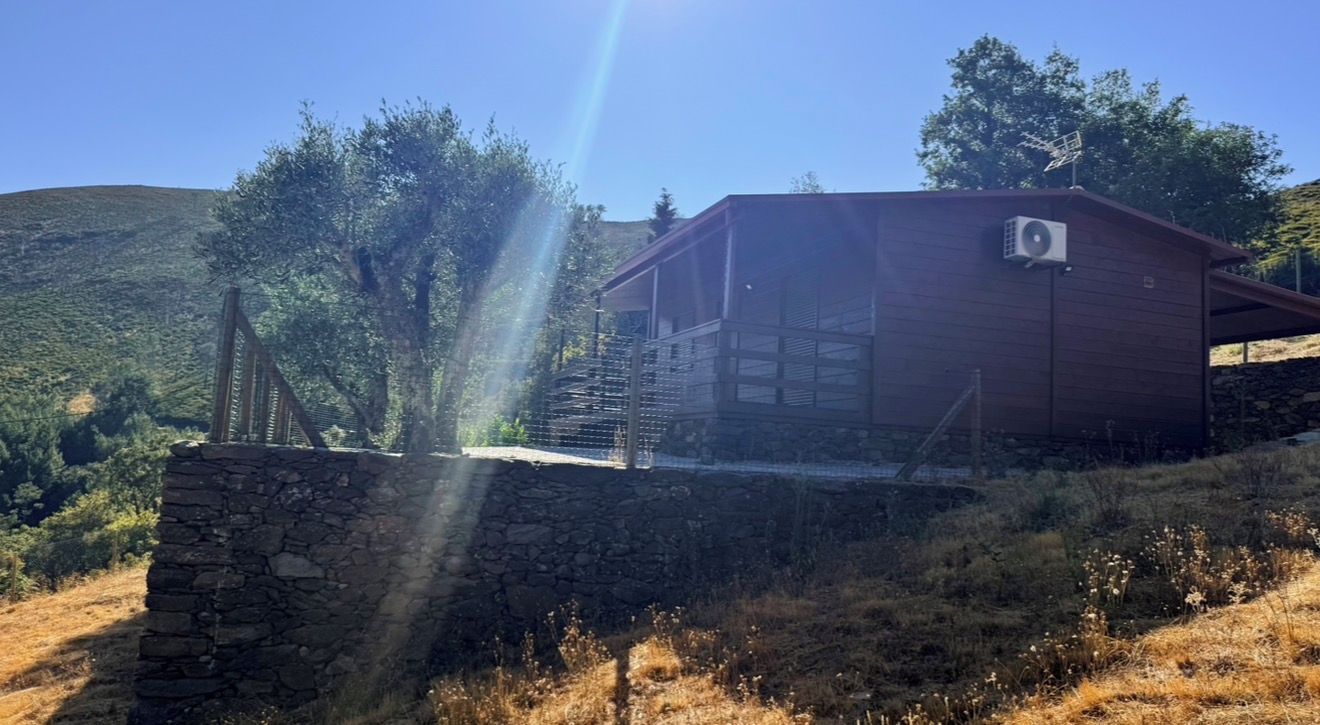 Une cabane rustique avec des fondations en pierres, une terrasse en bois et une vue dégagée sur les collines environnantes.