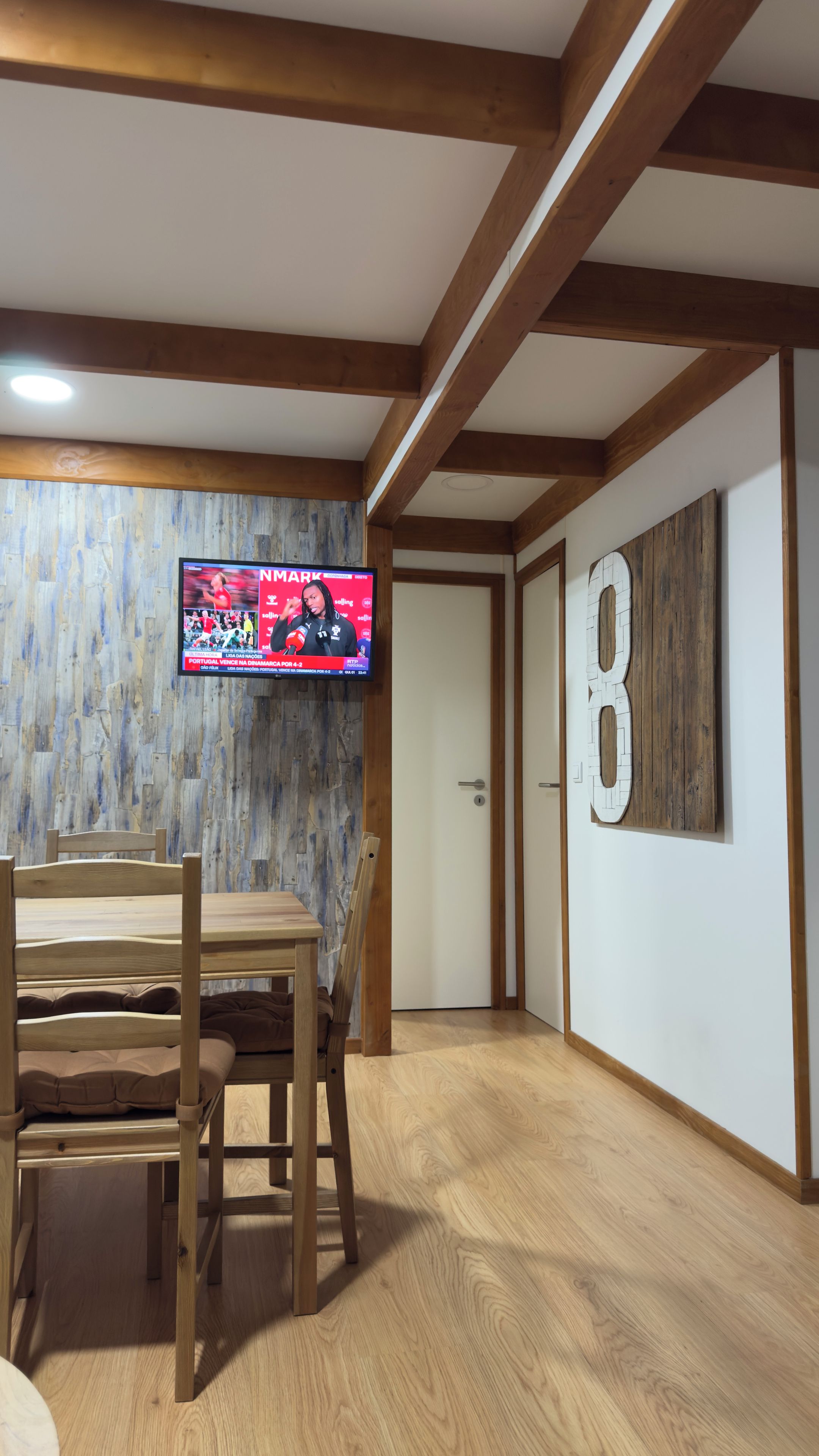 Una habitación con una mesa de comedor de madera, un televisor instalado en una pared de madera y una puerta con un adorno con el número 8.
