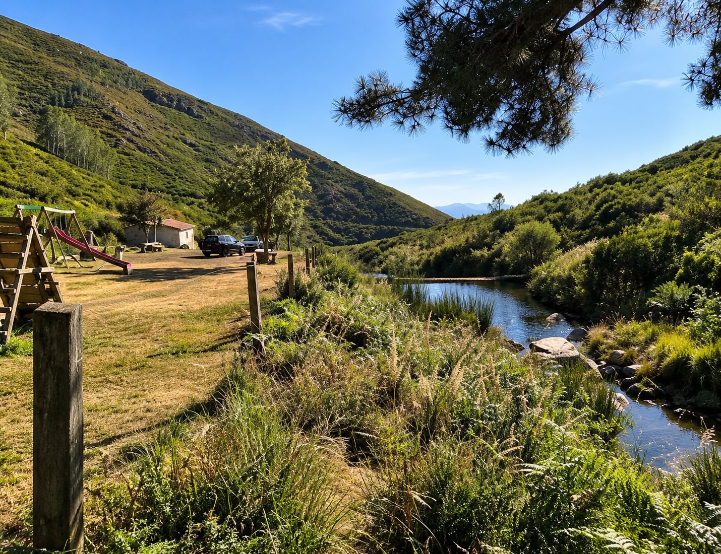 Paesaggio rurale con un fiume, un'area giochi e auto parcheggiate.