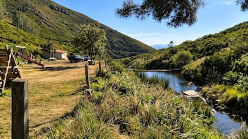 Paesaggio rurale con un fiume, un'area giochi e auto parcheggiate.