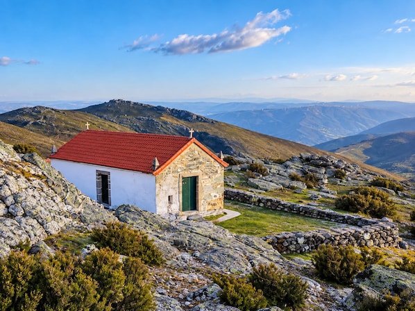 A small stone chapel with a red roof, surrounded by rocky terrain and sparse vegetation.