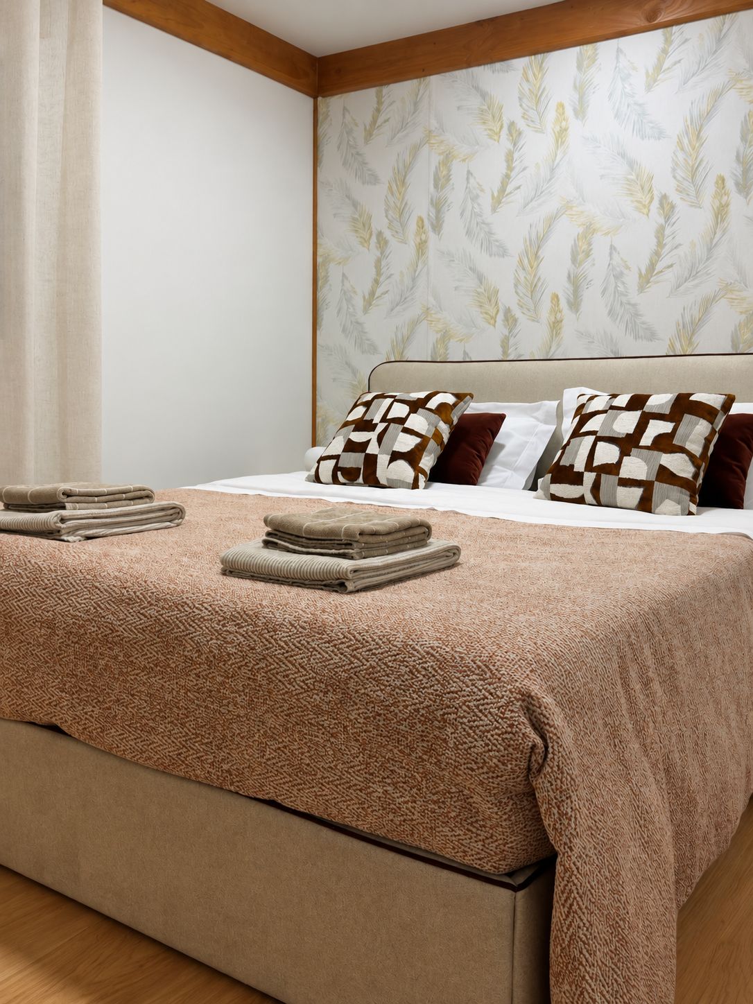A neatly made bed with a patterned bedspread, pillows, and folded towels.