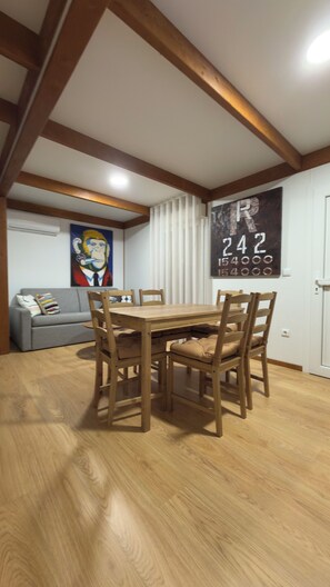 A dining area with a wooden table and chairs, a grey sofa, and a painting on the wall.