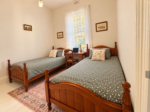 Een kamer met twee houten bedden, een bureau met een lamp en een raam met gordijnen.
