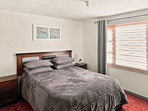 Un dormitorio con cama, mesita de noche y ventana con persianas.