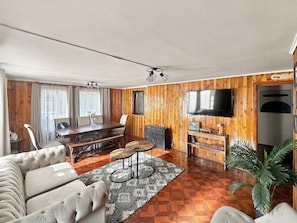 Una sala de estar con pared de madera, un televisor de pantalla plana, una mesa de comedor con sillas y un sofá.