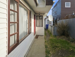 A narrow pathway leading to a house with a satellite dish, a red door, and a visible trash bin. - Oceana Suites General del Canto (punta arenas)