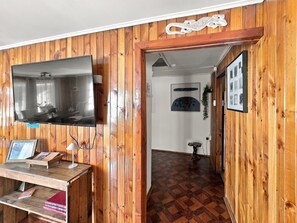 A room with wooden paneling, a flat-screen TV mounted on the wall, a wooden desk with a lamp, and a framed picture. - Oceana Suites General del Canto (punta arenas)