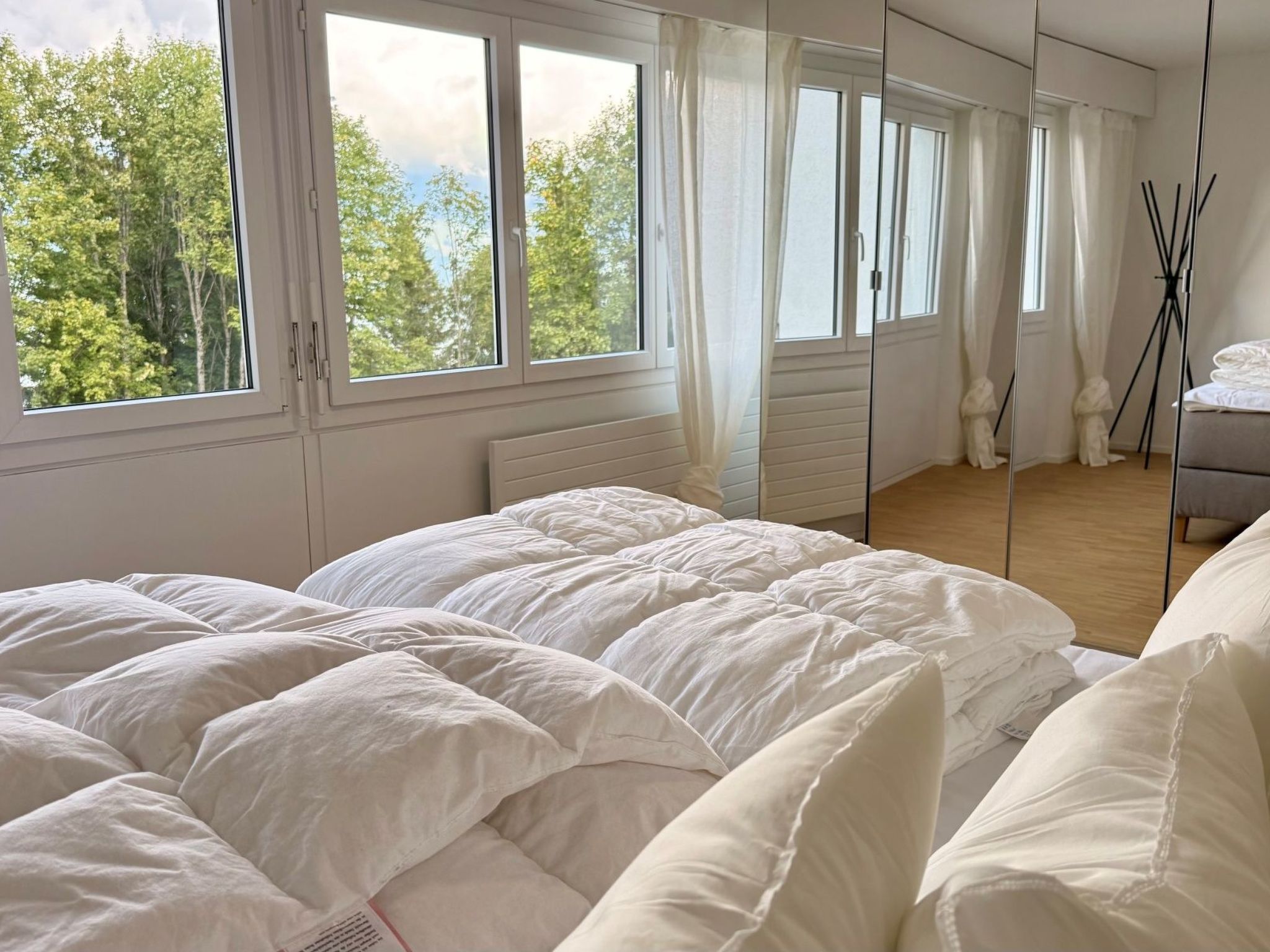 Un dormitorio con una cama grande, varias ventanas y vistas a árboles.